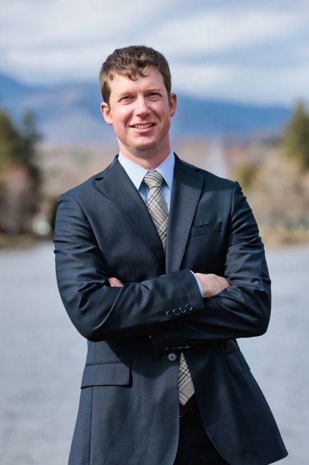 Barrett, a lawyer at Stone & Christy, poses in a suit with a sage green, plaid tie for a picture with the mountains in the background.