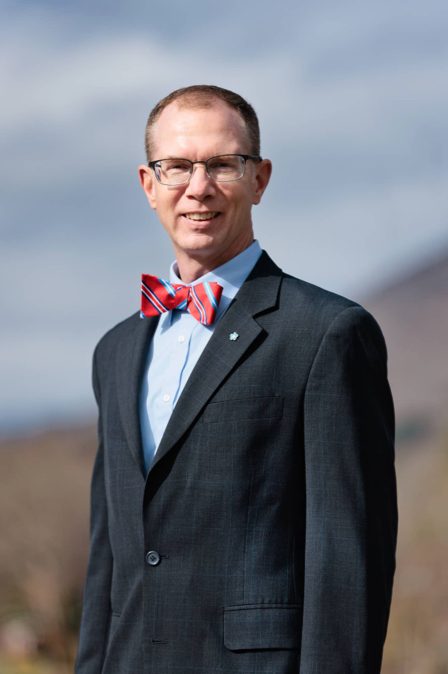 Bryant, a lawyer at Stone & Christy, poses in a suit and a red and blue striped bow tie for a picture with the mountains in the background.